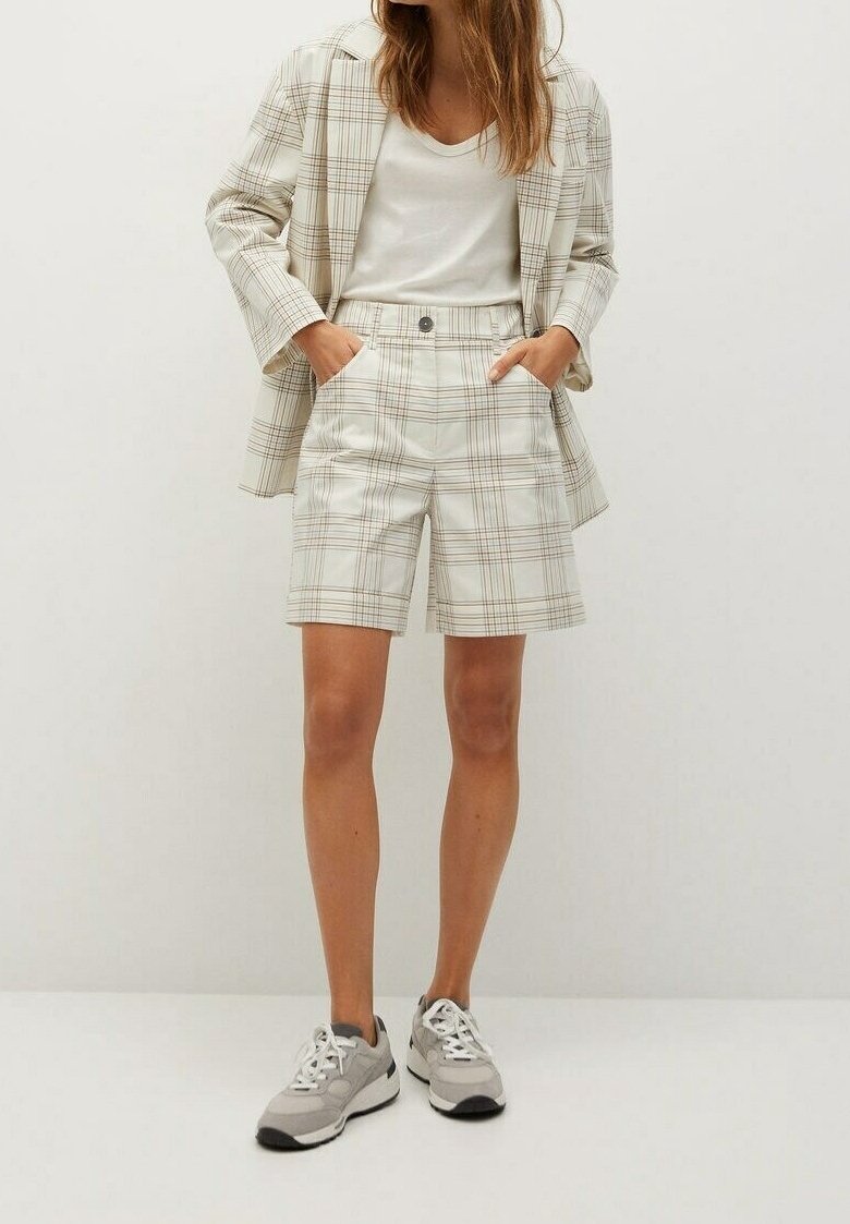 Blazer à carreaux léger et shorts assortis en crème avec des accents marron. T-shirt blanc décontracté et baskets grises. Texture de tissu lisse.