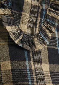 Karierter Stoff in Dunkelblau, Beige und Hellblau. Verfügt über einen gerafften Rand mit strukturierten Details und mehreren Mustern. Aus Baumwollmaterial.
