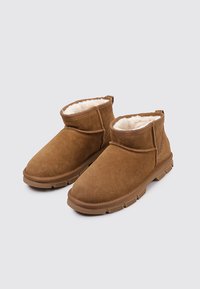 Braune Wildleder-Ankle Boots mit weichem cremefarbenem Fellfutter, Gummisohle und minimalen Nähdetails. Merkmale sind eine abgerundete Zehenpartie und ein mittelhoher Schnitt.