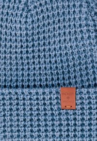 Wełniana czapka w kolorze jasnoniebieskim, z teksturowanym wzorem. Posiada brązową skórzaną metkę z wytłoczonym napisem "BICKLEY + MITCHELL".