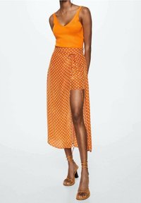 Oranje geribbelde tanktop gecombineerd met een maxi rok met stippen in een strik taille ontwerp, met een hoge split en sheer stof. Bruine bandjes sandalen.