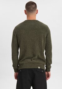Maglione lavorato a maglia verde oliva con scollo rotondo, polsini e orlo a costine, caratterizzato da un tessuto testurizzato. Indossato da una persona vista da dietro.