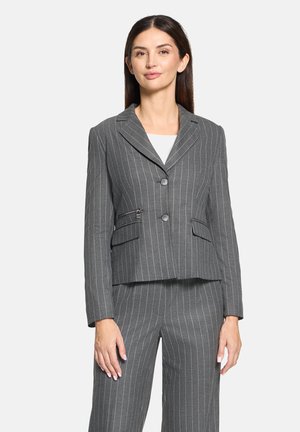 Grijze pinstripe blazer met een getailleerde pasvorm, inkeping kraag, twee voorzakken en knoopsluiting. Draagt over een witte top.