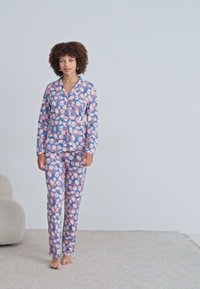 Pajama set s cvjetnim uzorkom u plavoj boji, s dugim rukavima i hlačama, izrađen od mekanog materijala s opuštenim krojem. Posebno ističe ružičaste cvjetne uzorke.