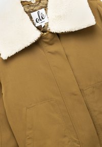 Beige buitenjas met een zachte beige kraag, voorzien van een ritssluiting en twee zakken aan de voorkant. Gladde stof met zichtbare binnenvoering.