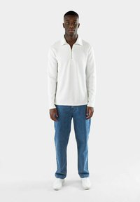 Vit långärmad tröja med dragkedja i kragen, kombinerad med ljusblå löst sittande jeans och vita sneakers. Enkelt och rent design.