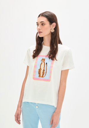 Camiseta blanca con un gráfico colorido de leopardo y texto en un diseño cuadrado. Combinada con pantalones azul claro, presenta un look casual.