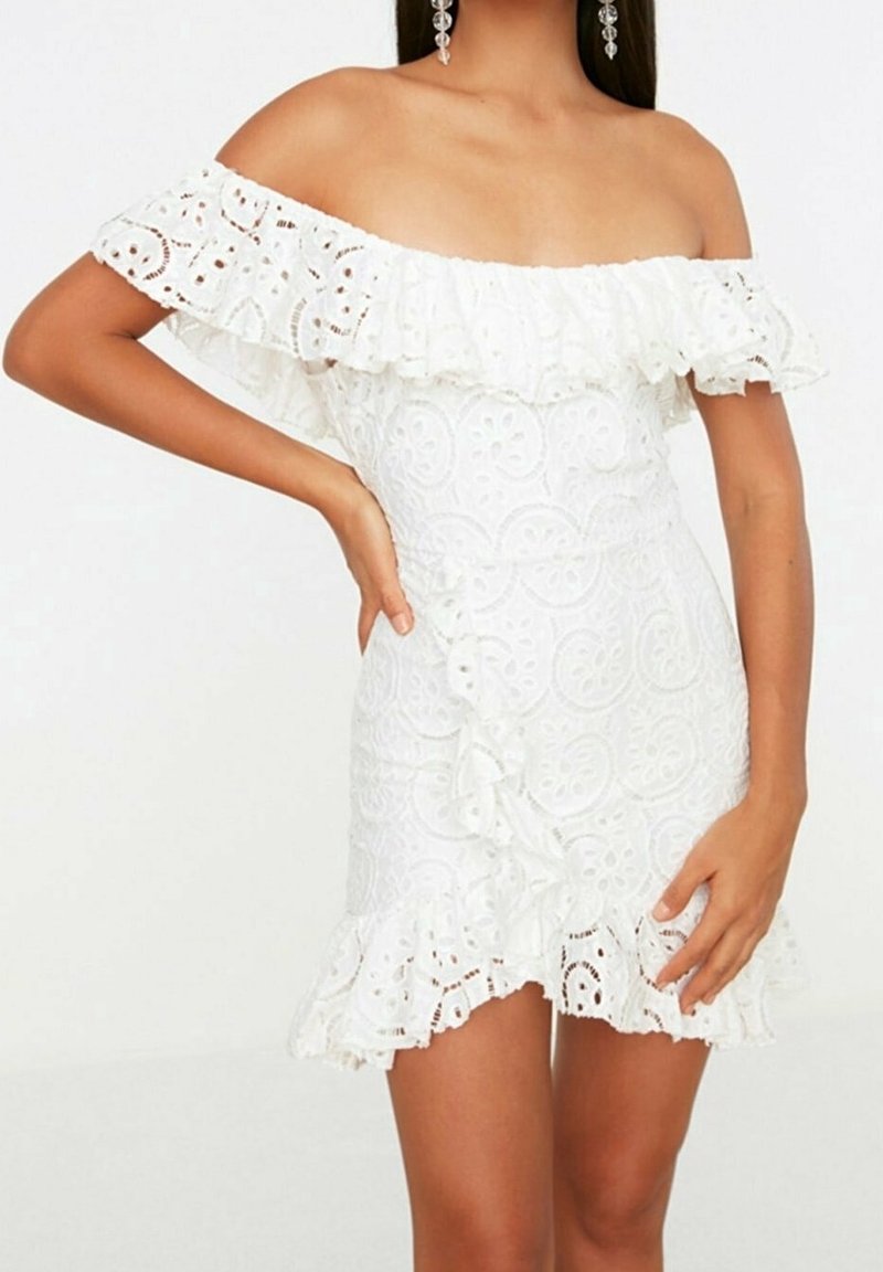 Valkoinen olkapäiltä paljaaksi jätettävä mekko, jossa on röyhelöhihoja ja tekstuurinen kuvio. Mekossa on liehukkeinen helma ja hienostunutta pitsikoristelua.