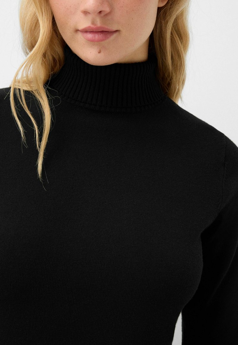 Schwarzer Rollkragenpullover aus einem weichen, strukturierten Strick. Merkmale einen hohen Kragen mit gerippten Kanten, taillierte Passform und lange Ärmel.