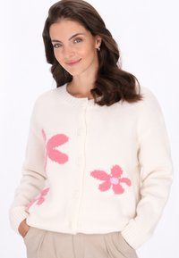 Bílý pletený cardigan s růžovými květinovými vzory, s kulatým výstřihem, zapínáním na knoflíky a strukturovanými rukávy.