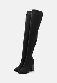 Bottes noires montantes au-dessus du genou en tissu extensible, avec un talon carré et une bande supérieure côtelée pour une meilleure adhérence et un confort accru.