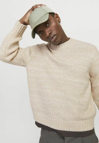 Beige knitted sweater with a ribbed neckline and cuffs, paired with a light green cap. The texture appears soft and cozy.