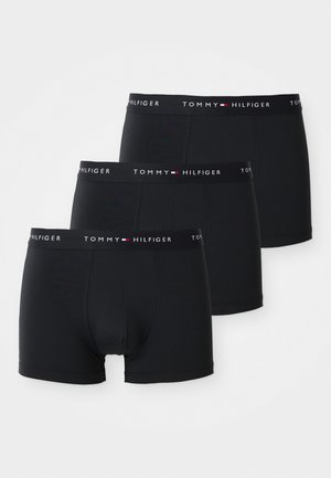 Drie zwarte Tommy Hilfiger boxershorts met gebreide elastische taillebanden gestapeld tegen een witte achtergrond.