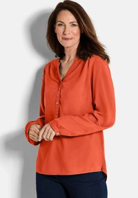 Orange Bluse mit langen Ärmeln, V-Ausschnitt und Knopfleiste. Weicher Stoff mit glatter Textur, mit seitlichen Schlitzen am Saum.