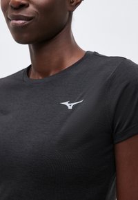 Κοντινό πλάνο ατόμου που φοράει σκούρο γκρι μπλουζάκι με στρογγυλή λαιμόκοψη και μικρό λευκό λογότυπο Mizuno στο στήθος.