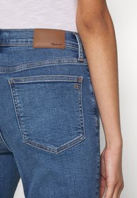 Tmavě modré džíny s rovnými nohavicemi, s hnědou koženou nášivkou v pase a dvojitě šitými zadními kapsami.