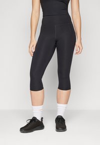Svarta capri leggings i stretchmaterial med hög midja och platta sömmar. Kombinerade med svarta träningsskor och vita strumpor.