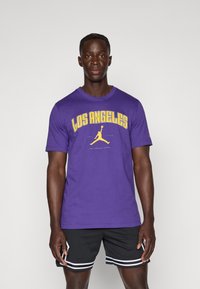 Violets krāsas T-krekls ar īsām piedurknēm, uz kura ir rakstīts "LOS ANGELES" dzeltenā krāsā un melns Jordan logo. Apvienots ar melniem šortiem ar baltām svītrām.