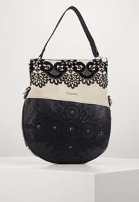 Czarna i beżowa torebka z misterną czarną koronką i wypukłymi wzorami, o gładkiej fakturze i krótkim czarnym pasku.
