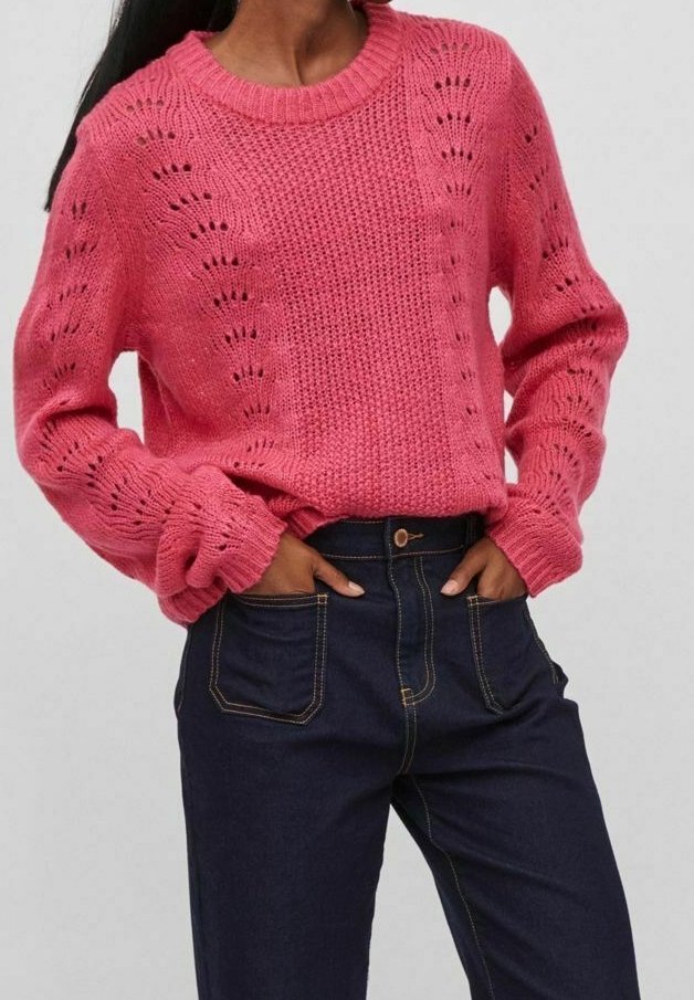 Maglione lavorato a maglia rosa con un motivo testurizzato, scollatura rotonda e maniche voluminose, abbinato a jeans alti di colore blu scuro.