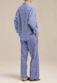 Niebieski zestaw odzieży domowej w wzory, składający się z długiego rękawa i luźnych spodni, obie części ozdobione skomplikowanymi wzorami paisley i charakteryzujące się swobodnym krojem.