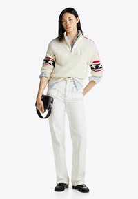 Grubo pleciony sweter z pół zamkiem, z kolorowymi wzorzystymi paskami na rękawach; w zestawieniu z białymi dżinsami i małą czarną torebką.