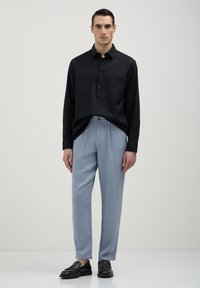 Chemise noire à manches longues avec boutonnière à l'avant, accompagnée de pantalons plissés bleu clair et de mocassins noirs. Design simple et épuré.