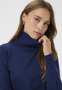 Pull col roulé bleu marine en maille côtelée, présentant un col montant et des poignets ajustés, avec une texture lisse et une coupe décontractée.