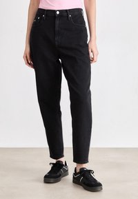 Vaqueros de mezclilla negros de alta cintura, con piernas ajustadas y estilo de cinco bolsillos. Combinados con zapatillas negras y una camiseta rosa ajustada.
