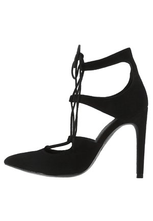 Sort højhælet sko lavet af blødt ruskind, med åben tå, krydset remdesign og spids tå med en blank sål.
