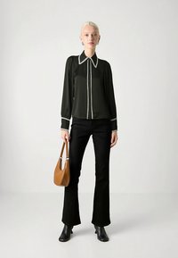 Svart blus med vita kantdetaljer, långa ärmar, knäppt fram, kombinerad med svarta utsvängda byxor och en brun axelväska.