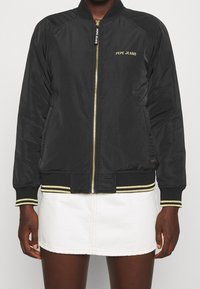 Černá bomber bunda se zlatými akcenty, zapínání na zip, žebrovaný límec a manžety, s vyšitým nápisem "PEPE JEANS" ve zlaté barvě na hrudi.