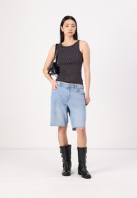 Top preto sem mangas com bolinhas brancas, calções de ganga azul claro e botas pretas até ao joelho com fivelas. A modelo carrega uma pequena bolsa preta.