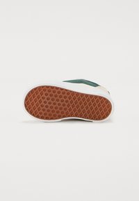 Gumowa podeszwa sneakersów z teksturowanym wzorem. Posiada białą zewnętrzną krawędź oraz brązową powierzchnię gripu w kształcie plastra miodu. Kontrast kolorystyczny z zieloną cholewką.