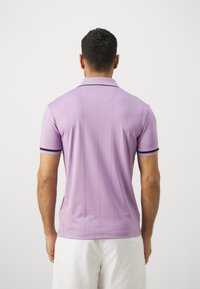 Violet polo marškiniai su trumpomis rankovėmis, turintys juodą apykaklės apdailą ir vertikalių juostelių dizainą. Lygi tekstūra, prigludusi forma.