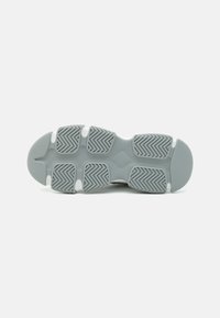 Semelle de sneaker grise en caoutchouc texturé avec un motif en chevrons, bout rond et accents blancs pour l'adhérence et la traction.
