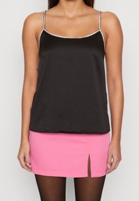 Camisole en satin noir avec des bordures argentées, associé à une mini-jupe rose ajustée dotée d'une fente sur le côté. L'ensemble du textile semble lisse.