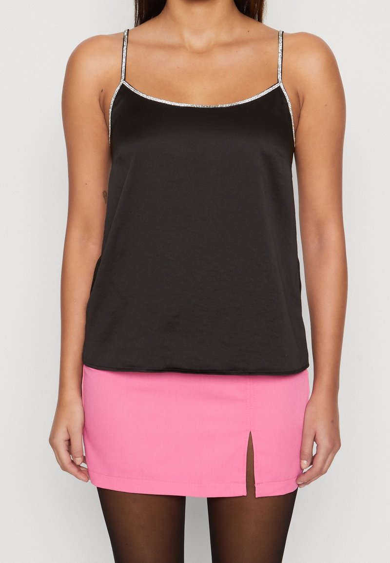 Camisole en satin noir avec des bordures argentées, associé à une mini-jupe rose ajustée dotée d'une fente sur le côté. L'ensemble du textile semble lisse.