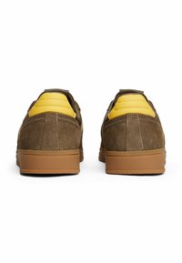 Braune Wildleder-Sneaker mit gelben Lederakzenten und einer hellbraunen Gummisohle. Verfügt über einen gepolsterten Kragen und eine strukturierte Oberfläche für besseren Halt.