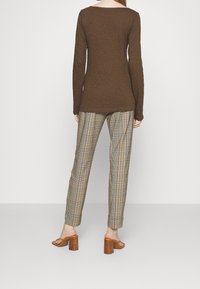 Ruskea pitkähihainen paita ja ruudulliset housut, joissa on vaaleanbeigejä, ruskeita ja mustia sävyjä; ruskeat korkokengät; kangas näyttää olevan teksturoitua.