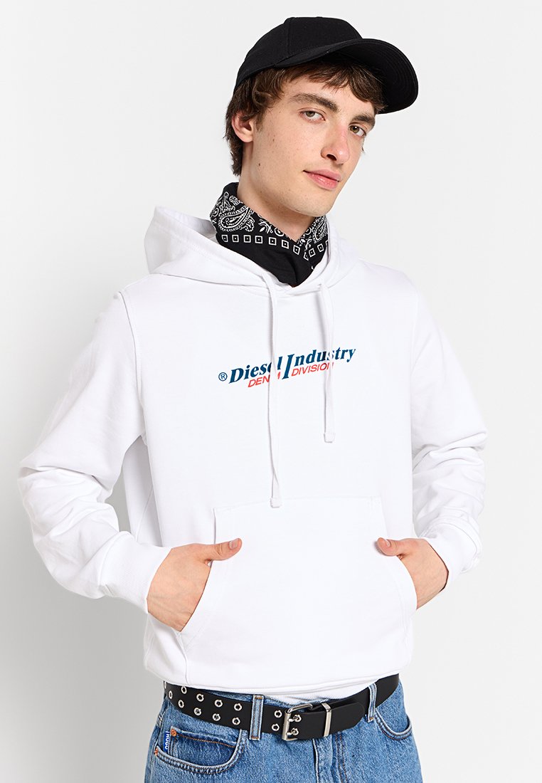 Felpa bianca con cappuccio e tasca frontale, con un logo blu e rosso. Indossata con un bandana nera e pantaloni di jeans, completata da un cappellino nero.