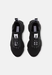 Black athletic shoes with a mesh upper, rubber sole, and elastic laces. Features a white brand label on the tongue and a looped heel tab.