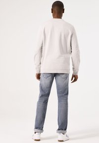 Sudadera gris claro con puños y dobladillo acanalados, combinada con jeans de mezclilla azul claro. Corte ajustado y diseño casual.