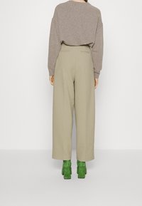 Beige wijde pantalons met een hoge taille, gecombineerd met een losse grijze trui en groene suède blokhak schoenen. Achteraanzicht.
