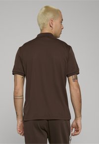 Brązowa koszulka polo z krótkim rękawem, wykonana z gładkiej tkaniny, z klasycznym kołnierzykiem. Posiada podwinięte rękawy i luźny krój.