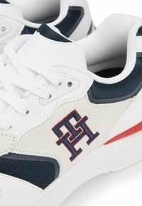 Zapatillas deportivas blancas con detalles en malla y ante en color marino. Incluye cordones blancos, un emblema rojo y una suela de goma texturizada.