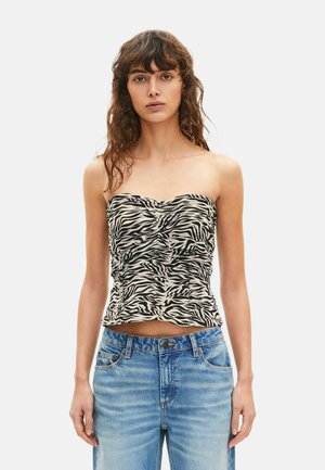 Ung kvinde med bølget hår iført en stropløs top med zebramønster og lyseblå jeans mod en ensfarvet baggrund.