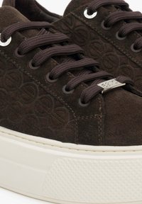 Brązowe zamszowe trampki z wytłaczanym wzorem, okrągłymi brązowymi sznurowadłami, srebrnymi oczkami i białą gumową podeszwą z teksturowanymi akcentami.