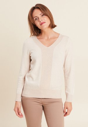 Pull en V color beige avec un panneau central texturé, des poignets et un ourlet côtelés, et une finition douce. Associé à un pantalon marron clair.