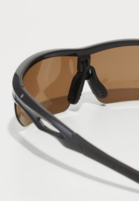 Sport glasögon med en stilren svart ram, bruna tonade linser, justerbara näskuddar och ventilerad design för luftflöde.